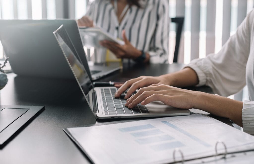 A cropped shot of two people working on laptops with documents for enterprise CMS