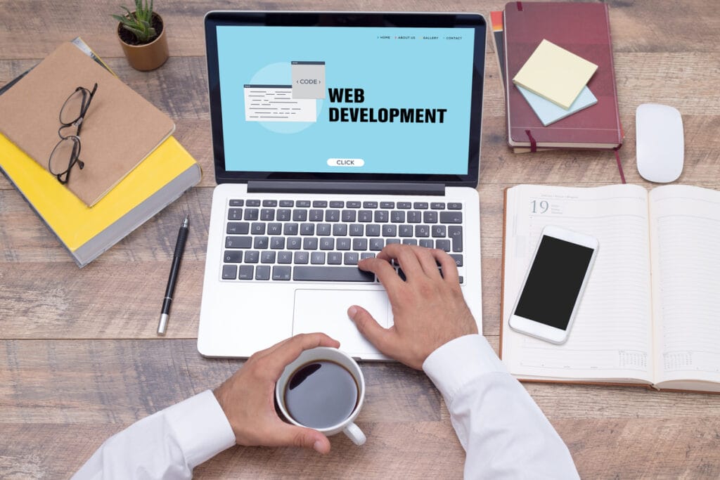 A cropped shot of one hand of a web developer on the laptop showing a web development concept and another hand on a coffee cup