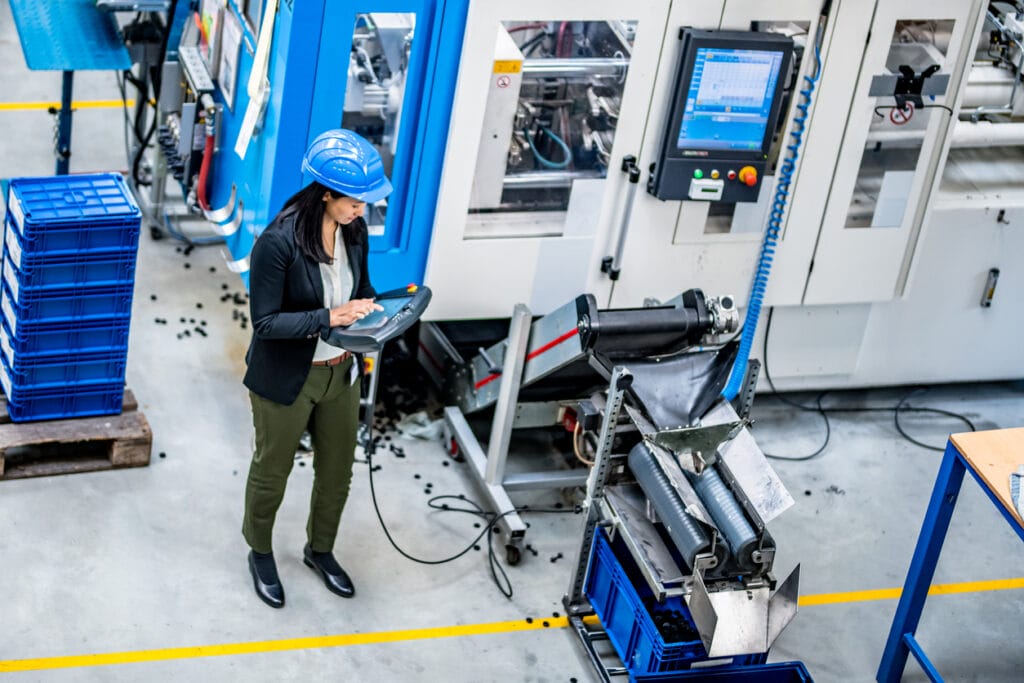 Web platforms for manufacturers: Elevated view of a female engineer operating manufacturing machinery with an industrial remote control in a factory.
